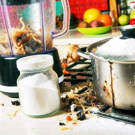 A kitchen scene with a pot of burnt noodles, a container of baking powder, a jar of salt, and a messy blender