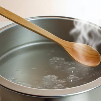 A wooden cooking spoon placed horizontally over a boiling pot of water